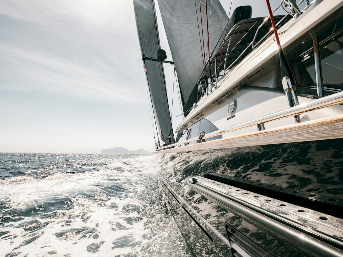 A close-up shot of a sailboat cutting through the water, with its sails catching the wind on a bright and sunny day at sea.